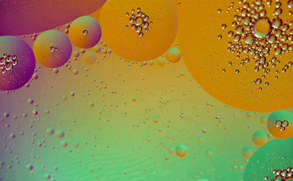 Gotas de aceite de distintos tamaños flotando sobre agua, vistas de cerca, con fondo de colores