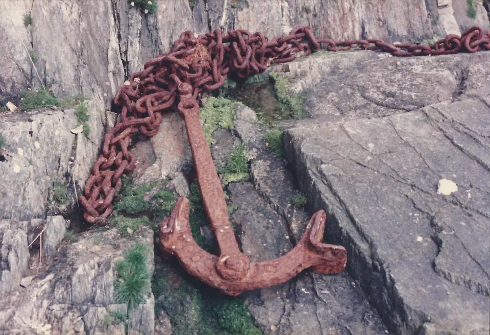 Ancla y cadena de hierro cubiertas de óxido rojizo, apoyadas sobre una roca