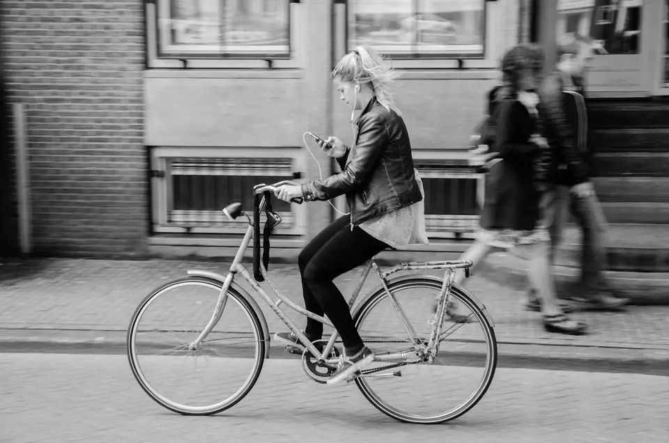 Mujer que avanza en bicicleta por una calle de Ámsterdam, vista de costado, en blanco y negro