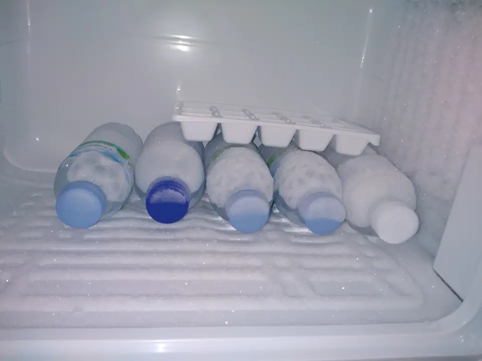 Interior de un congelador con botellas de agua acostadas y una cubetera con cubitos de hielo