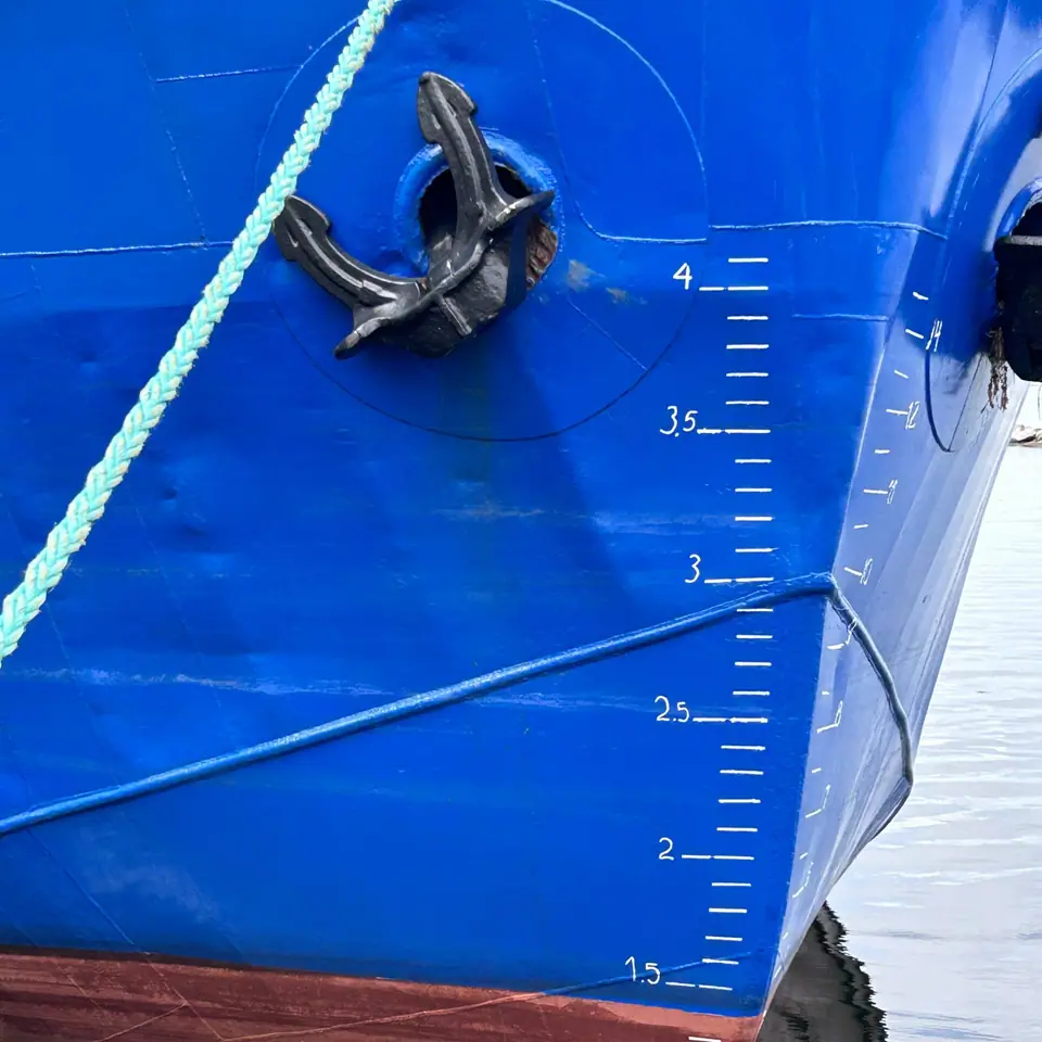 Proa azul de un barco de acero con las marcas de calado pintadas en metros, que indican cuánto se hunde el casco en el agua
