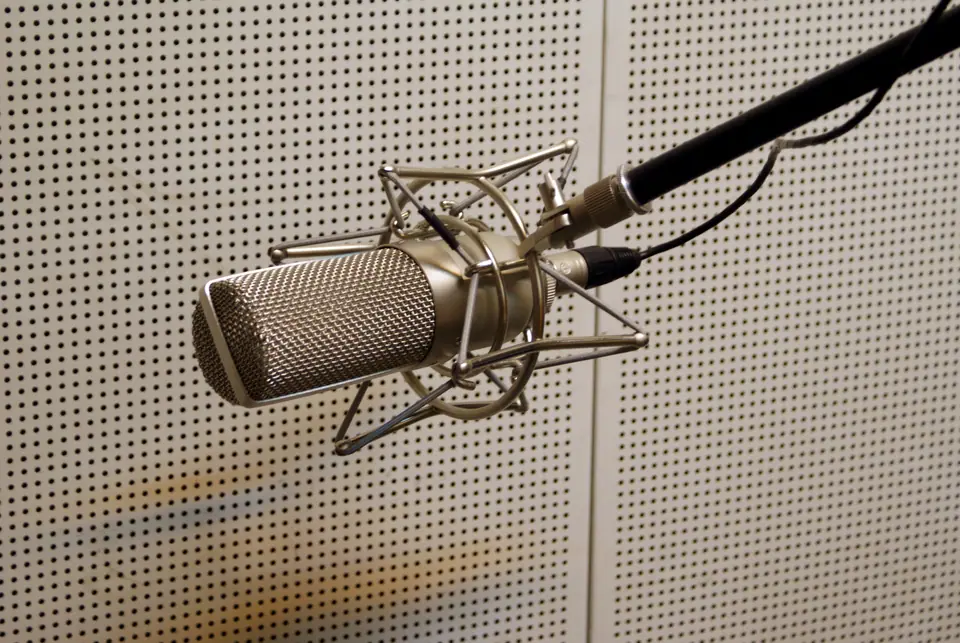 Micrófono de estudio en su soporte antivibración frente a una pared acústica perforada
