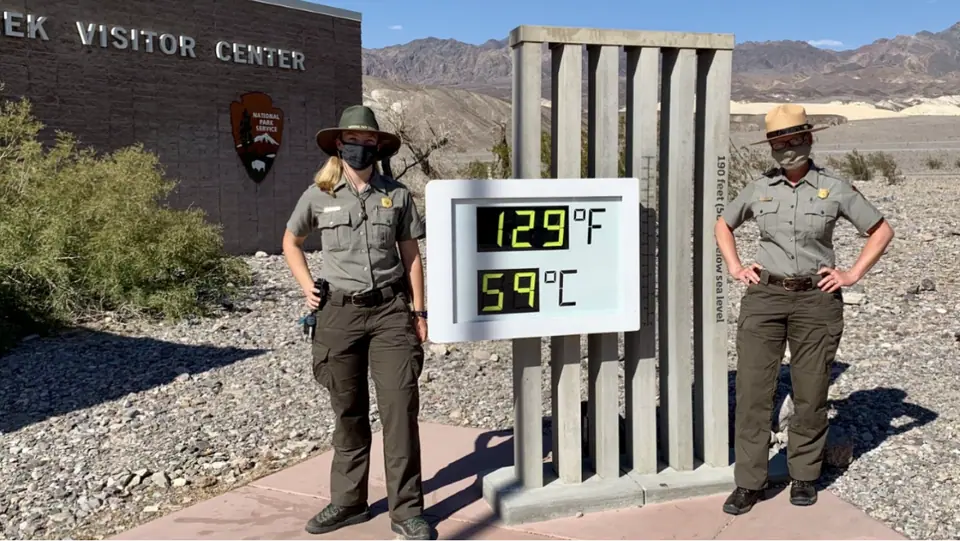 Dos guardaparques junto al termómetro gigante del centro de visitantes de Furnace Creek, en el Valle de la Muerte, que marca 129 °F (54 °C) en julio de 2020